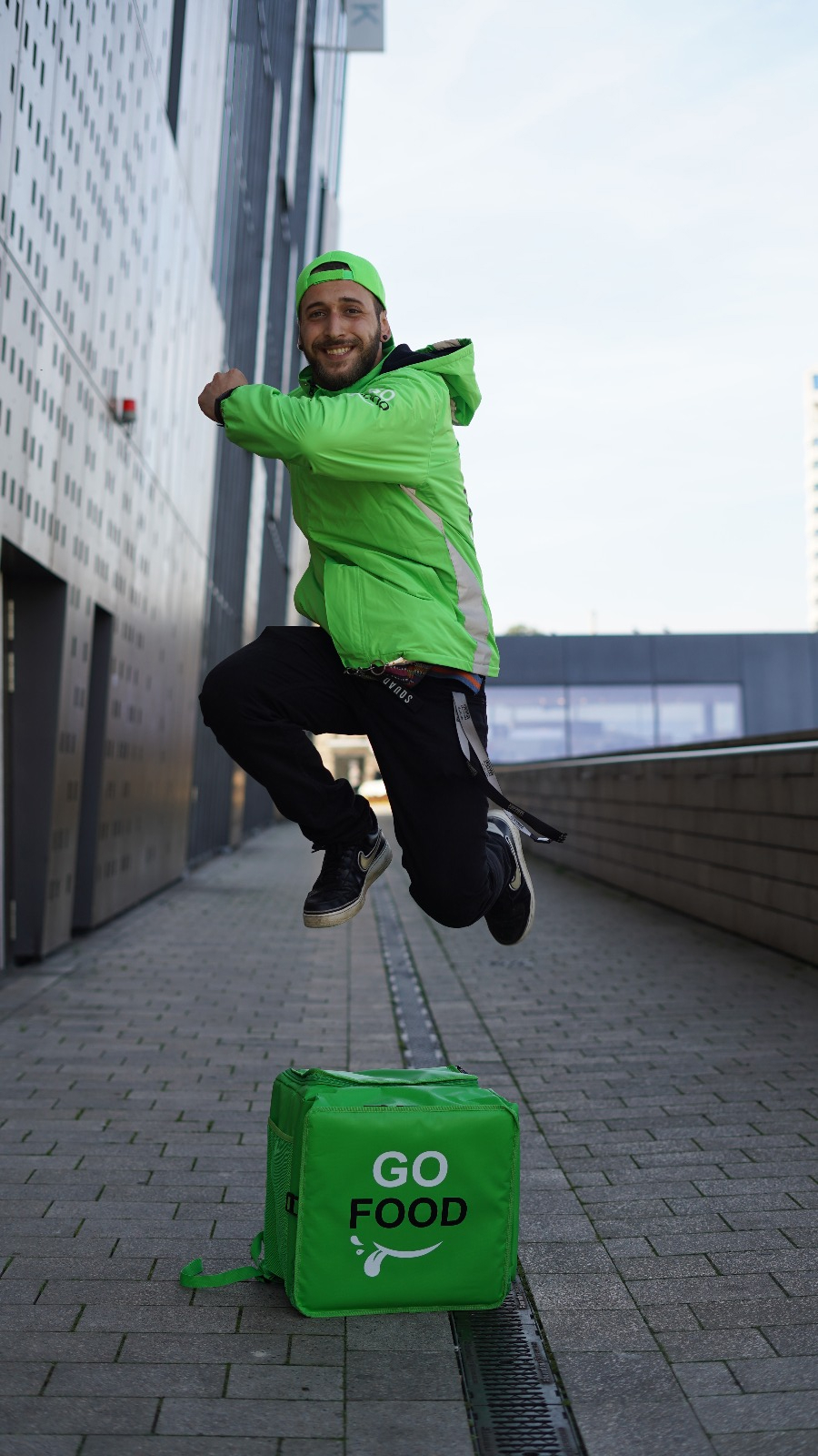Energetic GO FOOD delivery person captured mid-jump, showcasing the active lifestyle of urban food delivery services.
