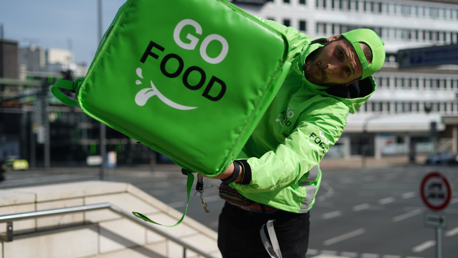 Delivery person in ‘GO FOOD’ attire on a bustling city street, indicating an active food delivery service in an urban setting.