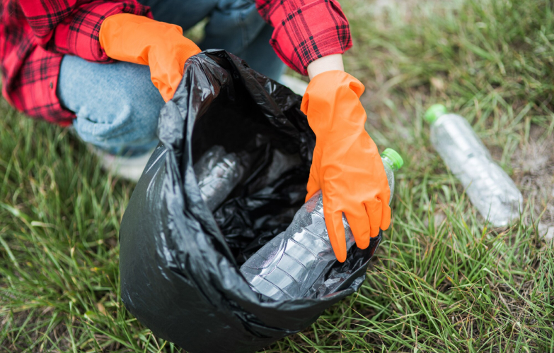 Person wearing gloves disposing of waste in a black garbage bag.
